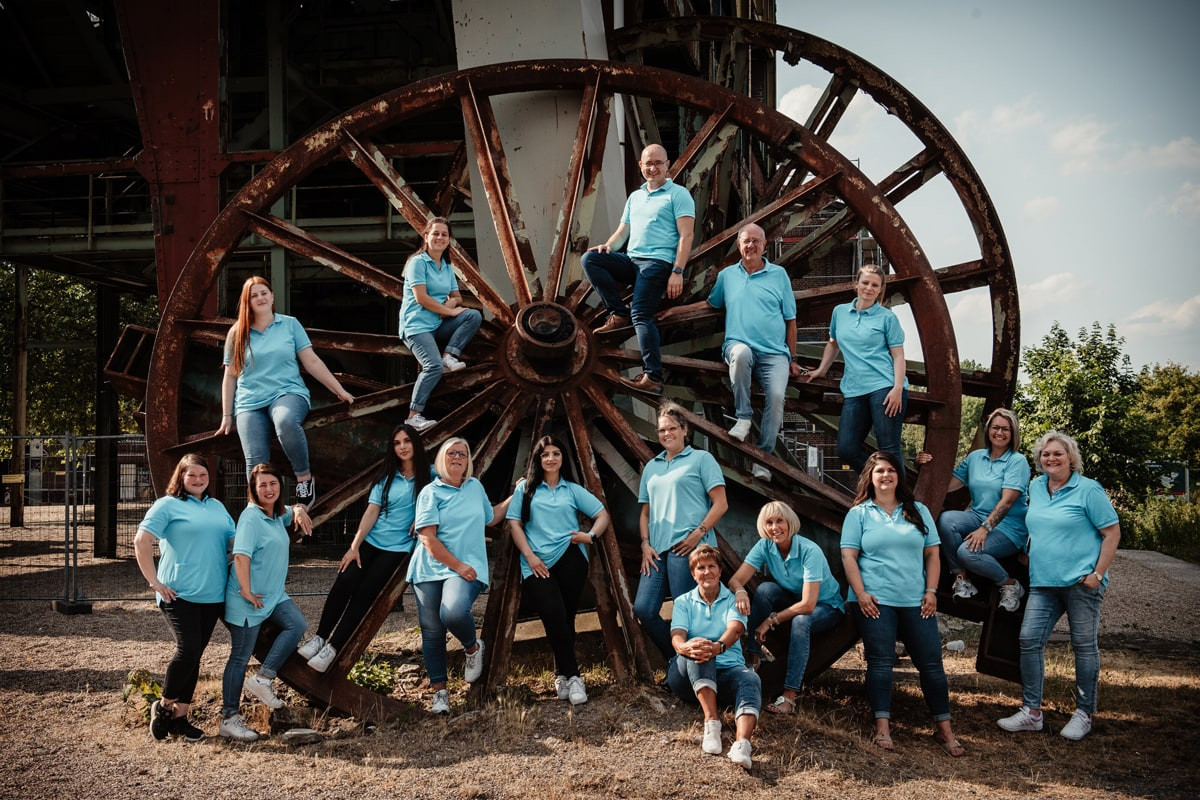 Team - Das komplette Team steht vor einem riesigen Holzrad